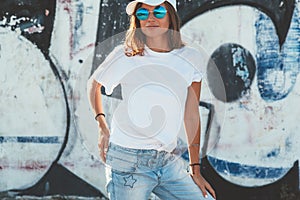 Model wearing plain tshirt and sunglasses posing over street wall