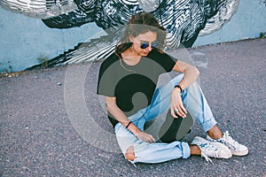 Model wearing plain tshirt and sunglasses posing over street wall