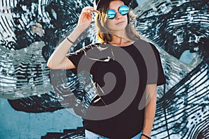 Model wearing plain tshirt and sunglasses posing over street wall