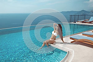 model in white bikini sunbathing by infinity swimming pool.