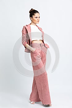 Model in white blouse, pink flared trousers with belt and jacket, white sandals with heels, with a silver chain around the neck, i