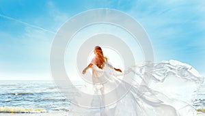 Model in White Dress Flying on Wind. Happy Woman Enjoying Sun looking away at Blue Sky. Carefree Girl dreaming at Sea Beach Resort