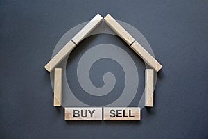 Model of a wooden house from wooden blocks. Words `buy sell`. Copy space. Business concept. Beautiful grey background