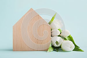 Model of wooden house and bouquet of white tulips on blue background close-up and copy space