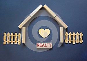 Model of a wooden house from wooden blocks. Word `realty`. Wooden heart and fence. Copy space. Business concept. Beautiful blue