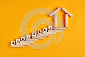Model of a wooden house and wooden stairway formed by wooden blocks with the word mortgage. Conept of buying a house with mortgage
