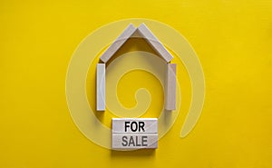 Model of a wooden house. Words `for sale` on wooden blocks. Copy space. Business concept. Beautiful yelllow background