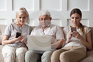 Modern adult family sit on couch using gadgets together