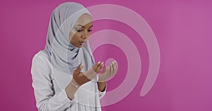 Modern African Muslim woman makes traditional prayer to God, keeps hands in praying gesture, wears traditional white