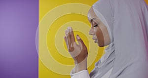 Modern African Muslim woman makes traditional prayer to God, keeps hands in praying gesture, wears traditional white