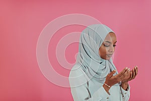 Modern African Muslim woman makes traditional prayer to God, keeps hands in praying gesture, wears traditional white