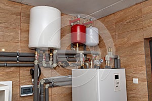 A modern air heat pump installed in the home\'s boiler room, visible plastic pipes and valves.