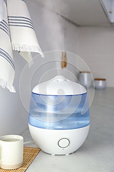 Modern air humidifier, cup and bamboo mat on counter in kitchen photo