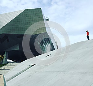 Modern angled glass and metal building with concrete slope and red shirt figure