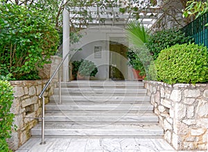 Modern apartment building entrance marble stairs, with potted plants and a glass door.