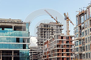 Modern apartment residential building glass facade wall construction site with many high tower cranes and heavy