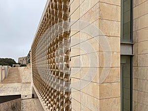 Modern architectural facade with geometric stone patterns creating depth and shadow. Beige limestone blocks form a