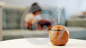 Modern aroma oil diffuser on the white table. Little boy in the background reading a book