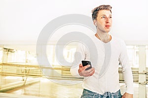 Modern art dancer dressed in white clothes listening a music with smartphone using a headphones in mirror hall