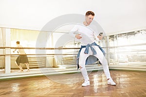 Modern art dancer teenager dressed in white clothes listening a music with smartphone using a headphones and dancing in mirror hal