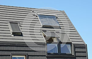 Modern attic roof with solar panels, skylights and blinds window for sun protection and house energy efficiency