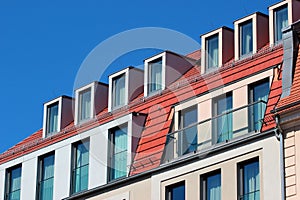 Modern attic windows on red roofs against blue sky background