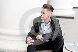 Modern attractive successful young man in a fashionable gray checkered jacket in a beautiful stylish shirt in jeans is resting