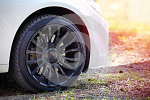 Modern auto wheel of car with beautiful black alloy disc and fresh rubber tread on rustic forest road with green grass on sunset