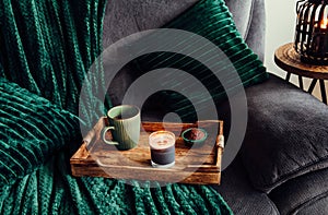 Modern autumn hygge set in living room. Dark green interior elements, soft pillows, plaid on sofa with chocolate muffin.
