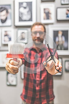 Modern barber holding cleaning brush and scissors at barbershop