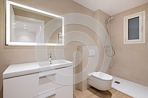 Modern bathroom with beige tiles, shower, toilet and rectangular large mirror with lighting