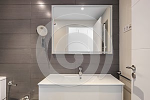 Modern bathroom with gray tiles, toilet and rectangular large mirror with lighting