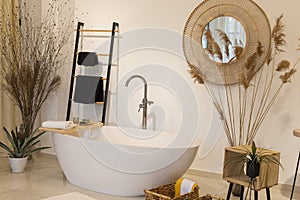 Modern bathroom interior with bathtub and water tap. Panoramic view of soap and clean towels, plant decorations, mirror, wooden