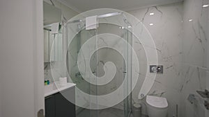 Modern bathroom interior showcases walk-in shower, glossy marble walls, sleek white fixtures, mirrored vanity in upscale