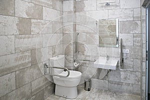 modern bathroom interior with white toilet, handicapped rails, white sink and mirror