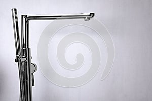 Modern bathtub faucet with hand shower on light grey background. Space for text