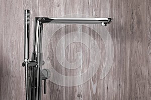 Modern bathtub faucet with hand shower on wooden background. Space for text