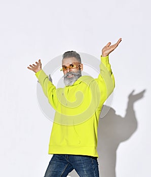 Modern bearded middle aged man hipster in yellow hoodie and glasses stands with hands up spread open palms. Copy space.