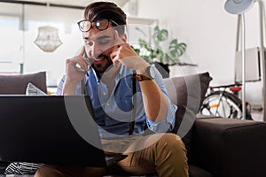 Young businessman working on laptop computer while sitting on sofa at home