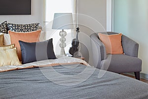 Modern bedroom interior with orange pillow on grey chair and bedside table lamp