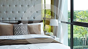 Modern bedroom beside window in the morning, pillows and cushions in white, beige and brown color tone on bed in luxury bedroom