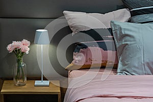 Modern bedside table bed lamp in cozy bedroom with pink carnations flowers in a glass bottle and modern fabric pillows interior