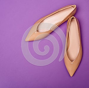 Modern beige female pointed-toe flat shoes isolated on a bright purple background.
