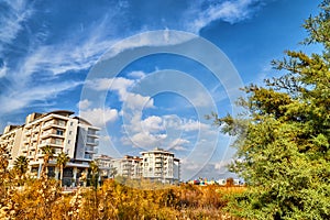 Modern big building, tree and greenery on foreground and blue sky on background. Hotel of block of flats is surrounded by green