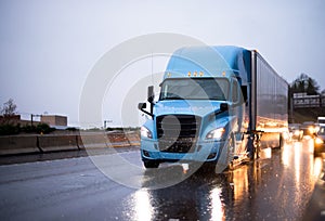 Modern big rig blue semi truck with trailer driving on rainy wet