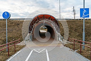 A modern bike path with markings and road signs. The bicycle road runs through a tunnel through a busy highway. A recreation area