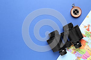 Modern binoculars, compass and world map on blue background, flat lay. space for text