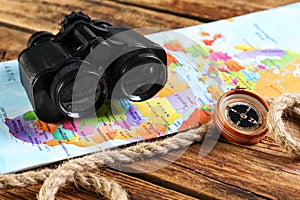Modern binoculars, map, compass and rope on wooden table