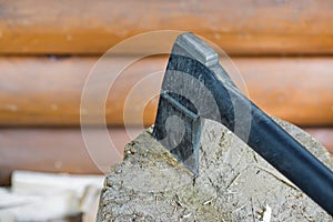 Modern black axe in the log and wooden chips after cutting firewood for winter near pile wooden house