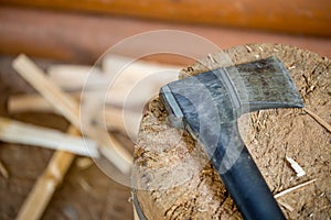 Modern black axe in the log and wooden chips after cutting firewood for winter near pile wooden house